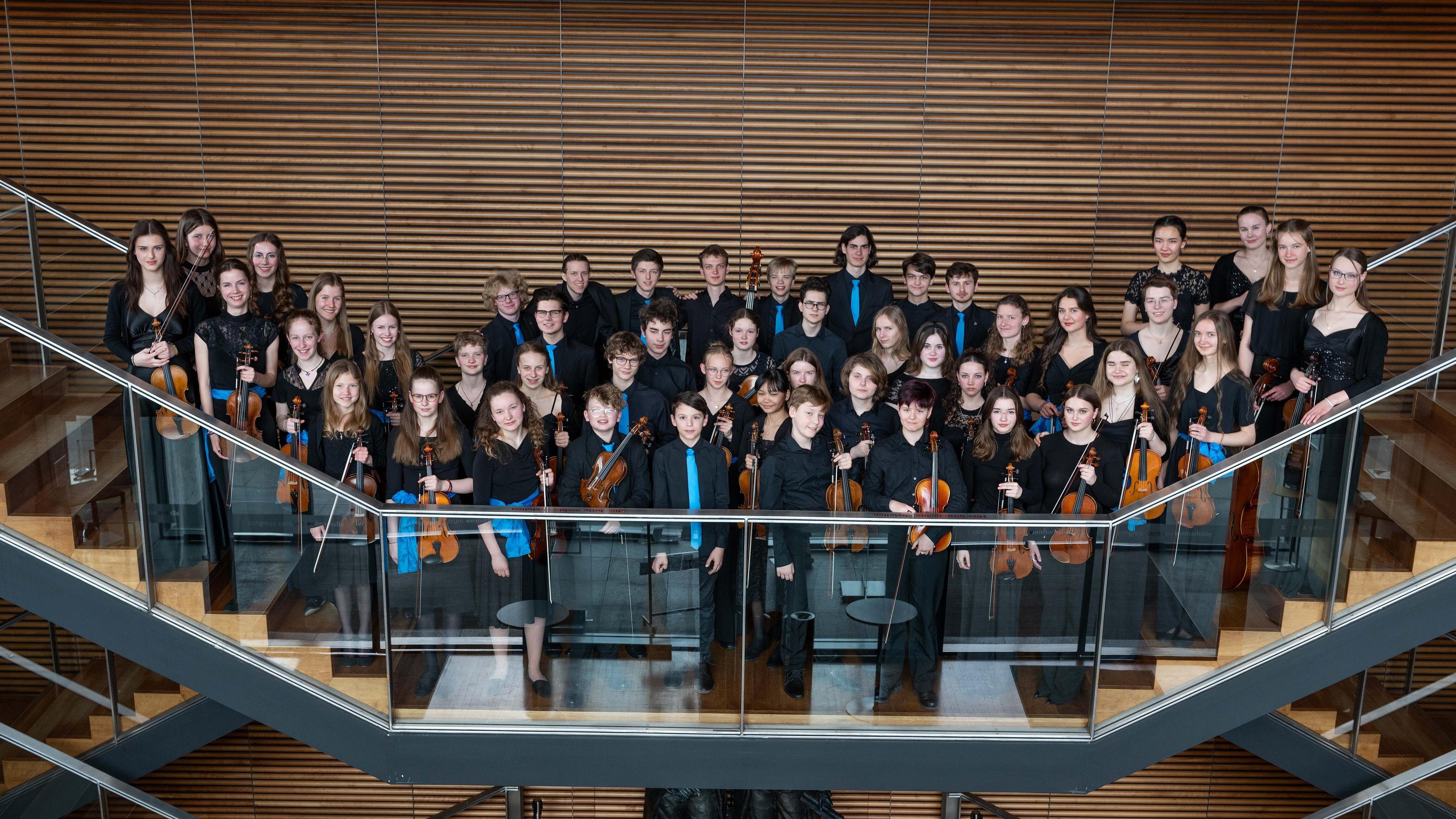 Die Orchestermitglieder posieren für das Gruppenbild in Konzertkleidung und mit Instrumenten in der Hand.